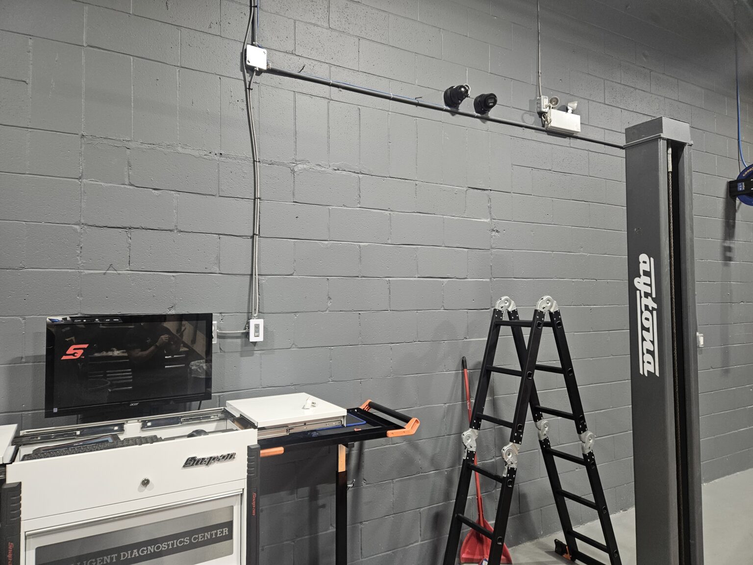 Two security cameras mounted on a block wall with clean conduit runs in an Ottawa auto shop